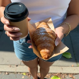 a person holding a croissant and a coffee